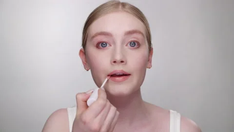 Makeup Tutorial: Beautiful female model applies lip gloss in mirror Stock Footage 193700431