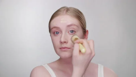 Makeup Tutorial: Blonde model blends in foundation around face with brush Stock Footage 193678202