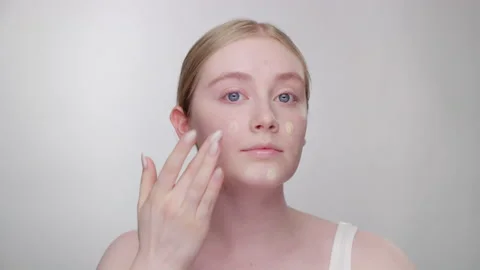 Makeup Tutorial: Blonde model dabs foundation around face with fingers 스톡 동영상 193670499
