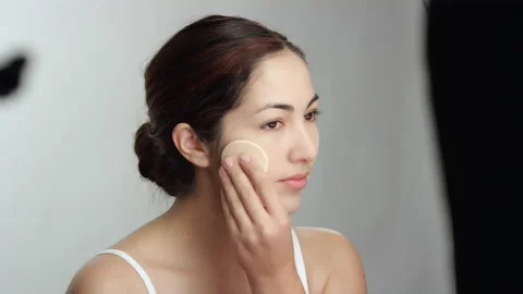 Makeup tutorial: Brunette model on white backdrop uses pressed powder forehead Stock Footage 193857842