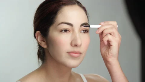 Makeup tutorial: gorgeous hispanic woman in studio uses eyebrow brush 스톡 동영상 193880303