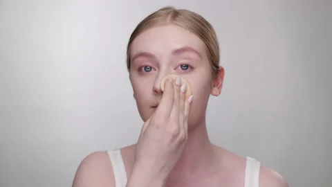 Makeup Tutorial: Pretty woman applies powder to face with sponge applicator Stock Footage 193676932