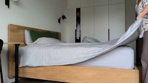 Making bed in cozy bedroom by spreading clean grey blanket over mattress su.. Stock Footage 346620463