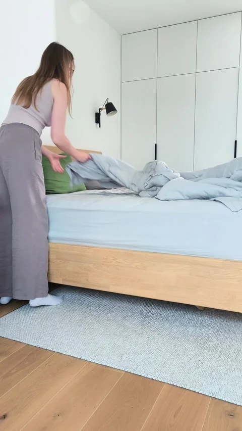 Making bed in a minimalist bedroom during morning housekeeping routine. You.. Stock Footage 345553272