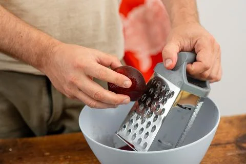 Making beet salad: hands with red beet juice using a metal grater. Stock Photos