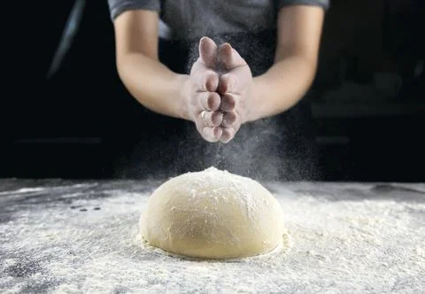 Making bread, kneading the dough. Hands on a dark background sprinkle flour on Stock Photos