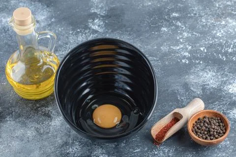 Making breakfast. Raw egg in black bowl with olive oil and spices Stock Photos