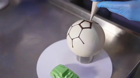 Making cake in a shape of soccer ball. Confectioner’s hands applying chocolate  Stock Footage 214028071