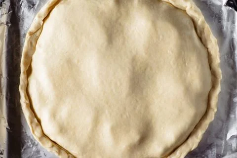 Making a closed pie. Round raw pie on a baking sheet. Top view. Stock Photos