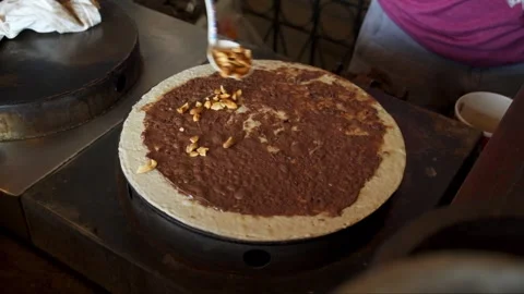 Making of crispy crepe filled with nutella and cashew nuts on crepe stove Stock Footage 277427385