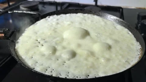 Making dosa on a hot pan in a kitchen with bubbles forming and cooking taking pl Stock Footage 328446119