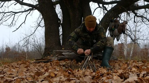 Making a fire by hunter in camouflage Stock Footage 100631098