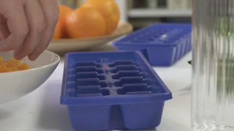 Making Ice Cubes With Small Pieces of Orange Fruits Stock Footage 106133616