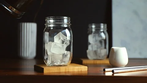 Making iced coffee. Pouring black coffee to a glass jar with ice cubes. Stock Footage 129806595