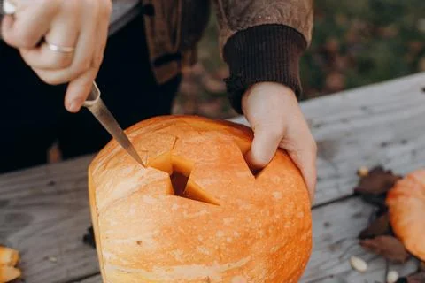 Making a jack o lantern. Hands carving halloween pumpkin on rustic wooden t.. Stock Photos