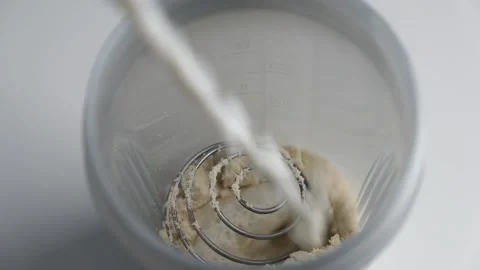 Making protein cocktail. Adding milk for protein powder into the shaker bottle Stock Footage 194059447