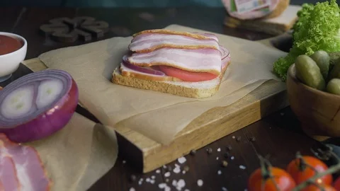 Making the sandwich with sliced bacon, pickle and vegetables on the wooden board Stock Footage 112827074