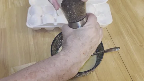 Making scrambled eggs. Hand twisting pepper grinder into bowl of raw eggs Stock Footage 340112334