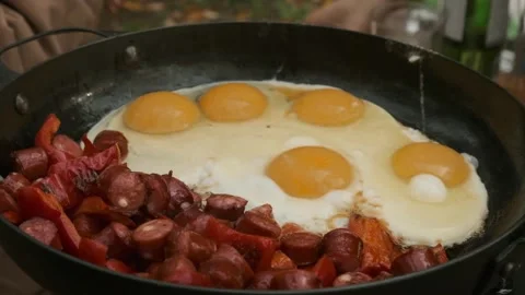 Making scrambled eggs with sausages in the stainless steel pan in nature Stock Footage 261141386
