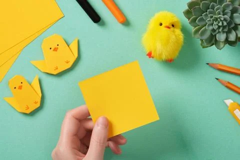Making a simple Easter origami handicraft. The hand holds a square piece of y Stock Photos