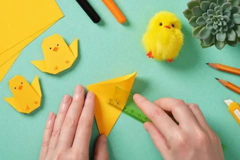Making a simple Easter origami handicraft. Hands fold a square yellow sheet i Stock Photos