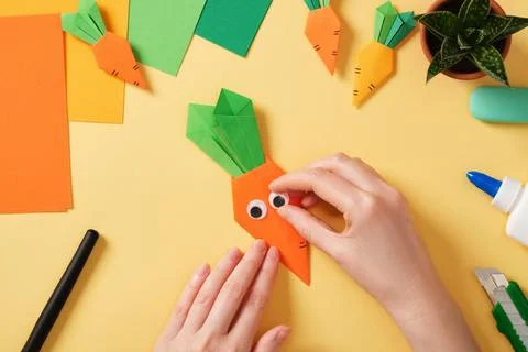 Making a simple origami carrot Easter craft. Glue on the funny eyes. Around.. Stock Photos