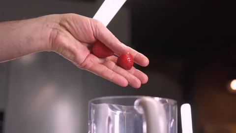 Making Smoothie in Blender. Hand throws strawberries in a blender. 库存影片 143415416