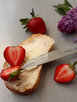 Making a snack with fresh bread, butter, and strawberries on a silver surface 스톡 사진