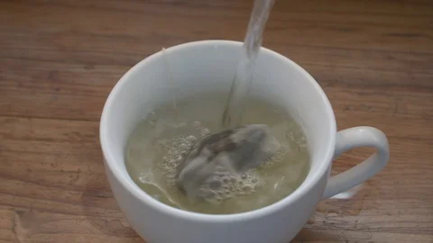 Making tea: hot water being poured in white cup with tea bag Video stock 94807189