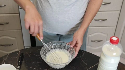 Making thin pancakes with milk. A pregnant woman makes pancakes in the kitchen a Stock Footage 317535671