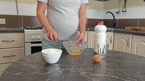Making thin pancakes with milk. A pregnant woman makes pancakes in the kitchen a Stock Footage 317536402