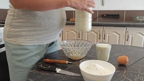 Making thin pancakes with milk. A pregnant woman makes pancakes in the kitchen a Stock Footage 317536630