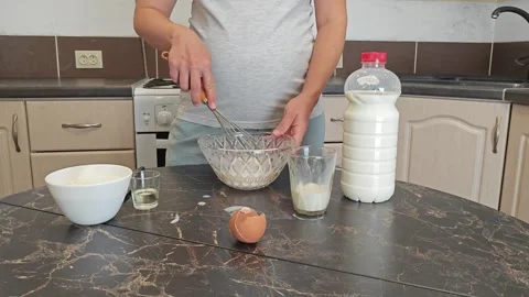 Making thin pancakes with milk. A pregnant woman makes pancakes in the kitchen a Stock Footage 317536680