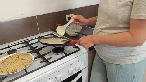 Making thin pancakes with milk. A pregnant woman makes pancakes in the kitchen a Stock Footage 317537455
