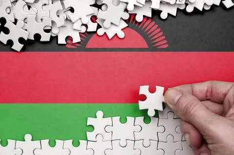 Malawi flag  is depicted on a table on which the human hand folds a puzzle of Foto stock
