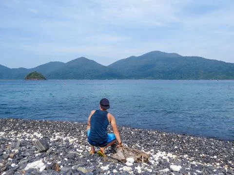 Malaysia - Man squating on the pebble beach Stock Photos