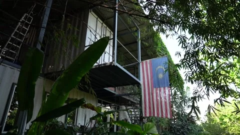 Malaysian flag hangs in the backdrop of office container overgrown with plants Stock Footage 270311911