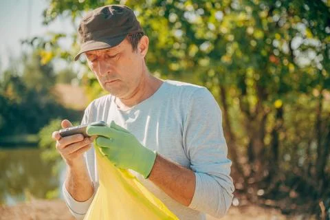 Male activist checking data on a mobile phone during a nature cleanup event.. Stock Photos