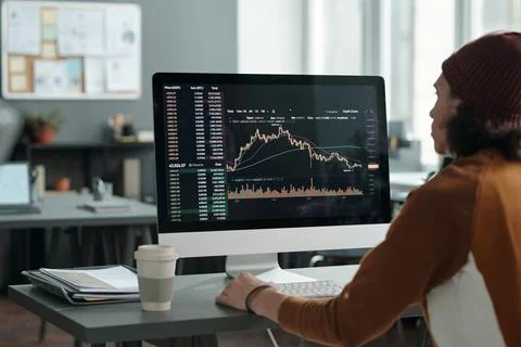 Male analyst sitting in front of computer monitor with graph on screen Stock Photos