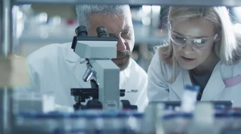 Male and female scientist are working with a microscope and a tablet in a lab Stock Footage