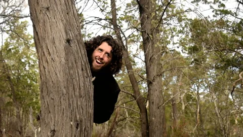 Male appears from behind a tree smiling. Stock Footage 196689580