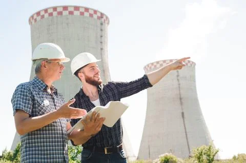 Male architects reviewing documents together at electric power plant. Stock Photos