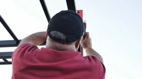 Male assembler of metal structures in a cap on his head tightens the nuts with Stock Footage 203593400