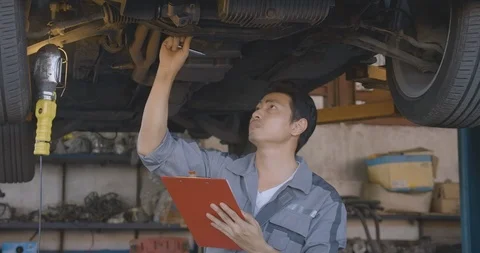 Male auto mechanic inspects the car undercarriage way in garage. Stock Footage