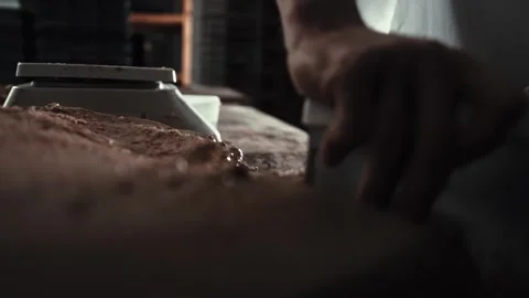 Male baker manually divides large mass of dough into blanks using scraper for Stock Footage 342230370