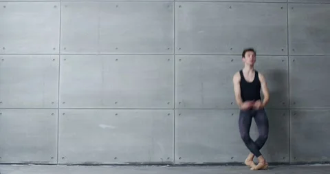 Male ballet dancer performs acrobatic elements of a ballet dance on a gray Stock Footage 144314991