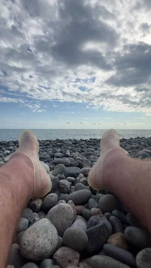 Male bare legs and feet in protective beach shoes on pebble coast Stock Footage 331173053
