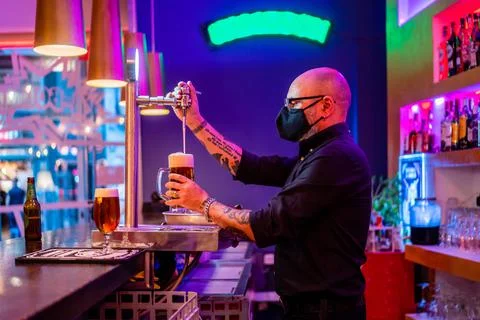 Male bartender in mask pouring alcoholic beverages in pub Stock Photos
