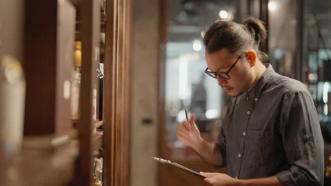 A male bartender is using a tablet to check product in a store. 스톡 동영상 202221882