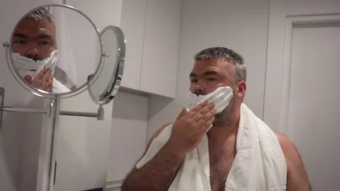 Male in bath bearded man. guy applies white foam. shaving gel on cheeks Stock Footage 239762782